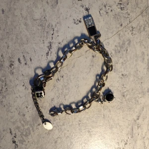 Chunky silverfärgat armband med berlocker - Stilrent chunky armband i silverfärg med coola berlocker, bland annat en tärning, svart sten och en rektangulär detalj med glittrande stenar. Perfekt accessoar för att lyfta din outfit.