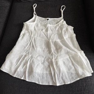Vit linnetopp med tunna axelband - Superfin vit linnetopp med tunna justerbara axelband och lätt rynkad struktur. Toppen har en luftig och flowy passform, perfekt för varma dagar. Materialet känns svalt och toppen har en lätt vågig nederkant som ger en avslappnad vibe.
