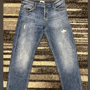 Jack & Jones Jeans - Snygga blå jeans från Jack & Jones med slitna detaljer och klassisk femficksmodell. Jeansen har raka ben, normal passform och knäppning med knappar. Jeansen är i storlek 36 34.  Perfekta för en avslappnad stil. Pris kan diskuteras vid snabb affär 