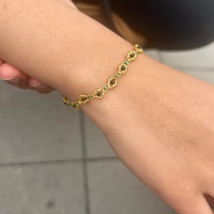Guldigt armband med gröna pärlor - Snyggt armband med små guldfärgade och gröna pärlor i ett blommigt mönster. 