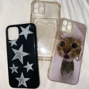 3 coola mobilskal med stjärnor & katt - Säljer tre mobilskal till iPhone 11 Pro. Ett svart skal med stora silvriga stjärnor, ett genomskinligt skal med plats för kort och ett transparent skal med en söt kattbild. Perfekt för dig som vill byta stil på mobilen ofta!