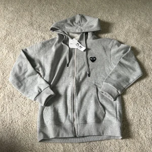 Comme des Garçons zip hoodie - Comme des Garçons Play zip-hoodie – grå med svart hjärta Säljer en helt ny hoodie med dragkedja från Comme des Garçons Play. Klassisk modell med det svarta hjärtat med ögon på bröstet. Endast provad – passade tyvärr inte mig.  ✔️ Storlek: M ✔️ Färg: Grå ✔️ Skick: Helt ny  Skicka meddelande vid frågor eller om du vill ha fler bilder!