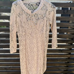 Ljus spetsklänning från Cream - Romantisk ljus spetsklänning från Cream med trekvartsärm och vackra paljett- och pärldetaljer vid halsringningen. Klänningen har blommigt spetsmönster och knappar framtill. Perfekt för dig som gillar en feminin och bohemisk stil.