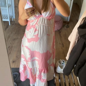 Rosa och vit långklänning H&M S - Supersöt långklänning från H&M i storlek S med rosa och vitt mönster. Klänningen har v-ringad omlott-topp, smala axelband och volang nertill. Perfekt för varma dagar och ger en chill sommarkänsla.