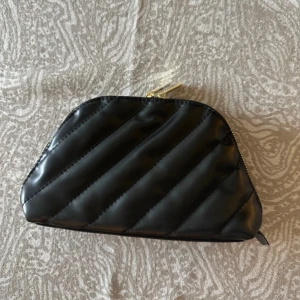 Svart quiltad necessär från YSL Beauté - Snygg svart quiltad necessär från YSL Beauté med guldfärgad dragkedja och logga på zip-pullern. Väskan har ett mjukt, glansigt material och elastiska innerfickor för smidig organisering av dina essentials. Perfekt att ha med i väskan eller på resan💖💖