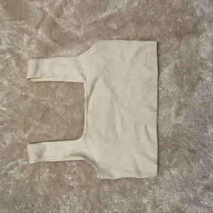 Vit croppad linnetopp från H&M - Säljer en stilren vit croppad linnetopp från H&M. Toppen har breda axelband och är ärmlös med en fyrkantig halsringning. Perfekt att matcha med jeans eller kjol för en clean look. Materialet är mjukt och stretchigt för en bekväm passform.