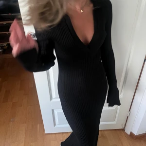 Svart ribbad långklänning med v-ringning - Svart långklänning i ribbstickat material med djup v-ringning och långa ärmar. Klänningen har en tight passform som framhäver figuren💘