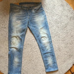  Dondup jeans - Säljer ett par ljusblå skinny jeans från Dondup med slitna detaljer och snyggt tvättad look. Jeansen har klassisk femficksdesign, orange sömmar och är tillverkade i bomull. Märkt med Dondup-patch bak och etikett från George Skinny Fit.