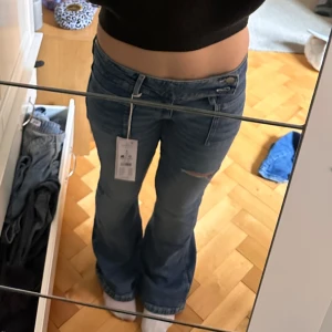 Blå bootcut jeans med slitningar - Trendiga Snygga blå bootcut jeans från ginatticot young med låg midja och slitningar på båda benen. Jeansen har klassiska fickor fram och bak samt en cool, lite sliten look. Perfekta för dig som gillar en avslappnad och trendig stil. Endast använda 1 gång