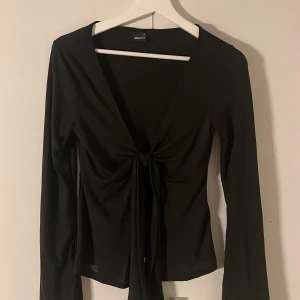 Svart omlottopp från Gina Tricot - Säljer en svart omlottopp från Gina Tricot med lång ärm och snygg knytning framtill. Passar till allt. Nästan helt oanvänd ❤️