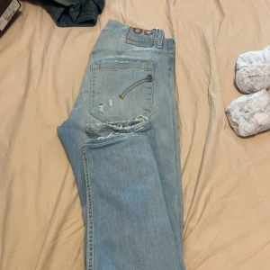 Dondup jeans - Säljer ett par ljusblå slim jeans från Dondup med slitningar och små hål på bakfickan. Jeansen har klassisk femficksdesign, låg midja och är tillverkade i mjukt denim. Perfekta för en avslappnad och trendig look. Sitter bra på mig som är 170 57 kg