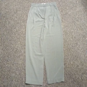 Ljusgrå kostymbyxor från H&M - Snygga ljusgrå kostymbyxor från H&M i klassisk modell med hög midja och raka, vida ben. Byxorna har pressveck framtill, hällor för bälte och diskreta fickor bak. Perfekta för en clean och stilren look.