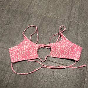 Rosa bikiniöverdel med vita prickar - Snygg rosa bikiniöverdel med vita prickar och justerbara axelband. Modellen har en cool cut-out detalj framtill och knäpps med spänne i ryggen. Perfekt för stranden eller poolen! Materialet är stretchigt och bekvämt. Endast använd ca 1-2gånger