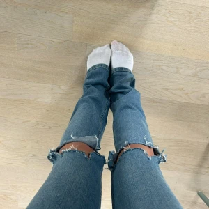 Blå ripped jeans med raka ben - Säljer ett par ljusblå jeans med raka ben och stora slitningar vid knäna. Jeansen har klassisk femficksdesign och är i ett mjukt denimtyg. Perfekta för en avslappnad och trendig look.💗💗