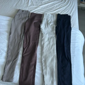 Ribbade leggings i olika färger - Säljer flera par ribbade leggings med hög midja i olika färger: beige, brun, vit, marinblå, ljusgrå och ljusgrön. De är stretchiga och sitter tight, perfekta för en chill och sportig look. Materialet är mjukt och skönt, troligen polyester eller bomullsmix. 20kr styck