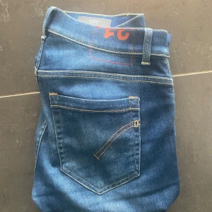 Dondup George  - Snygga blå jeans från dondup i storlek 31. Modellen är slim och skinny med klassisk femficksdesign och kontrastsömmar. Jeansen har en mörkblå tvätt och är tillverkade i stretchigt jeansmaterial som sitter tajt och bekvämt. Perfekt för dig som gillar en modern och smal siluett.