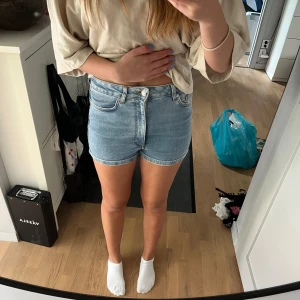 Ljusblå jeansshorts  - Snygga ljusblå jeansshorts från NA-KD x Pamela med klassisk femficksdesign, hög midja och uppvikta benslut. Shortsen har dragkedja och knapp framtill samt bälteshällor. De är i ett stretchigare material.