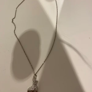 Halsband med skridsko-hänge i silver - Supersött halsband med ett glittrigt skridsko-hänge i silverfärg. Kedjan är tunn och smidig, och hänget är dekorerat med små stenar som ger extra bling. Perfekt för dig som älskar konståkning eller vill ha något unikt och sportigt runt halsen. Säljer för att jag passar inte i silver. 
