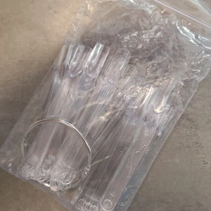 Genomskinliga nageltippar på ring - Ett set med genomskinliga nageltippar monterade på en metallring, perfekt för att visa upp olika nagellack eller nail art. Tipparna är av plast och har en klassisk oval form, smidiga att använda för swatches eller övning. Säljs i försluten plastpåse.