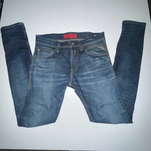Replay blå jeans strl 28 - Snygga blå jeans från Replay med klassisk femficksdesign och coola broderade detaljer på bakfickorna. Jeansen har kontrastsömmar och en röd Replay-etikett på insidan av linningen. Passformen är slim och materialet är slitstarkt.