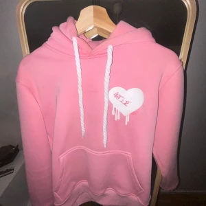 Rosa hoodie med hjärta och LOVE-tryck - Säljer en rosa hoodie från 4TTHELOVE med vit snörning och stor ficka framtill. På bröstet finns ett vitt hjärta med rosa text och droppande effekt, och på huvan står det LOVE i vitt. Mjuk insida och normal. Hade sagt att det passar XS-S. Priset kan diskuteras!🩷💞