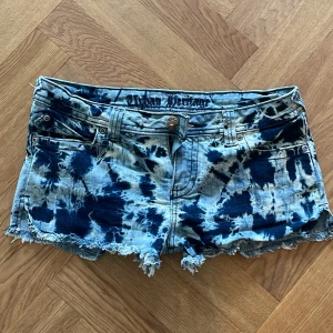 UNIKA LÅGMIDJADE JEANSSHORTS - Skitsnygga jeansshorts från Urban Heritage med blå och vita tie-dye-effekter. Modellen har låg midja, fransiga kanter och coola fickdetaljer med knappar bak. Köpt på beyond retro sparsamt använda säljs i befintligt skick se bilderna !