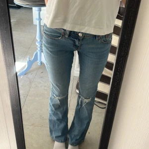 Blå bootcut jeans från Gina Tricot - Bootcut jeans från Gina tricot med låg midja och slitna detaljer vid knäna. Snygga bakfickor med sömmar och knapp. 