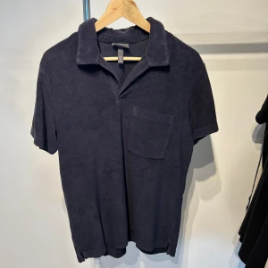 Mörkblå frotté t-shirt med krage - Snygg mörkblå t-shirt från H&M i mjuk frotté med klassisk krage och bröstficka. Perfekt för dig som gillar chill och avslappnad stil. Kortärmad modell med loose passform och enkel design som funkar till jeans eller shorts.