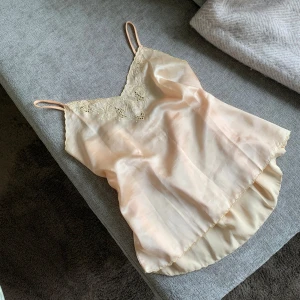 Champagnefärgad linnetopp med spets - Säljer en superfin linnetopp i champagnefärg med tunna axelband och v-ringad hals. Toppen har vacker spetsdetalj med blommönster framtill och är gjord i glansigt silkesliknande material. Perfekt för dig som gillar en romantisk och chic vibe.