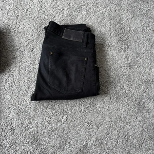 Svarta jeans Iggy 31/32 - Svarta jeans från tiger of Sweden Iggy i klassisk rak modell med fem fickor och snygga nitar vid bakfickorna. Jeansen har normal passform och är tillverkade i ett slitstarkt bomullsmaterial. Perfekt för dig som gillar stilrena och enkla svarta jeans.
