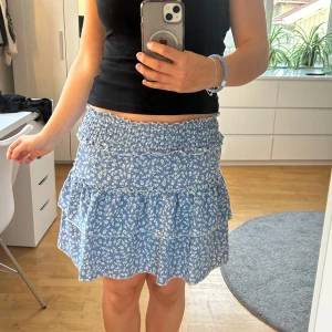 Kjol - Söt blå kjol med små vita blommor och volangdetaljer. Jättefint skick och nästan aldrig använd. Köpt för några år sedan och minns inte vart jag köpte den! Den har en elastisk midja för bekväm passform och därför skulle jag säga att den passar storlekar som S/M! Skriv om du har frågor! 💖