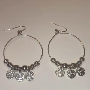 Silvriga creoler med glittriga berlocker - Snygga silvriga örhängen i creolmodell med runda pärlor och tre glittriga berlocker på varje örhänge. Perfekt för dig som gillar att sticka ut med lite extra bling. De är lätta och har en modern, rund form som passar till många olika stilar.