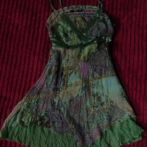 Grön paisley kortklänning från Gina - Säljer en färgstark grön kortklänning från Gina med paisley-mönster i lila, rosa och blå toner. Klänningen har omlott-v-ringning, smala axelband och paljettdekor vid bysten. Materialet är lätt och luftigt, perfekt för varma dagar. 💖💖💖Ej använd. 