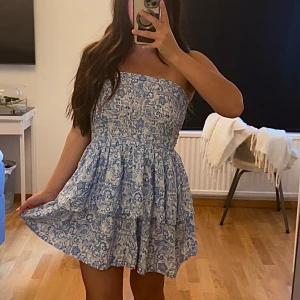 Blåvit mönstrad volangklänning  - Superpoppis blåvit klänning som har ett detaljerat blommigt mönster och volang i kjolen som ger en extra flowig känsla. Perfekt för varma dagar och sommarhäng med vänner. Aldrig använd. Storlek L men passar mig som har XS/S. 