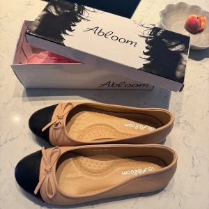 Beige och svarta ballerinaskor  - Snygga ballerinaskor köpta på raglady. Beigea med svart tå och söt rosettdetalj framtill. Har en  mjuk innersula.. Aldrig använda, helt nya