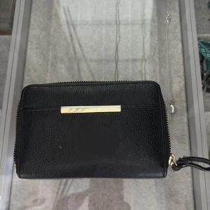Svart plånbok med gulddetalj - säljer en svart plånbok från okänt märke! jätte fin och lätt att ha med. svart skinn med guld detaljer