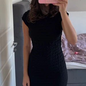 Svart kort klänning med öppen rygg - Säljer en svart, tight kortklänning med snygg struktur i tyget och öppen rygg. Klänningen har korta ärmar och sitter figurnära, perfekt för dig som gillar en stilren och cool look. Materialet känns mjukt och har en lätt stretch.