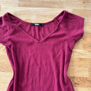 Vinröd ribbad topp från Bik Bok - Säljer en vinröd ribbad topp från Bik Bok i storlek S. Toppen har v-ringad hals, korta ärmar och är figurnära i modellen. Materialet är mjukt och stretchigt, perfekt för att ge en snygg siluett. Enkel att matcha med jeans eller kjol för en cool look. Något nopprig