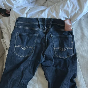 Mörkblå Replay jeans med kontrastsömmar - Snygga mörkblå jeans från Replay med klassisk femficksdesign och coola kontrastsömmar. Baktill finns stilrena broderade detaljer på fickorna och en brun läderpatch med Replay-logga. Jeansen har normal passform och är tillverkade i slitstarkt denim.