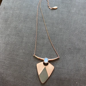 Geometriskt halsband från Pilgrim - Unikt halsband från Pilgrim med tunn kedja i roséguldston. Hängsmycket har en geometrisk form i beige och grått, samt en rund, skimrande blå sten upptill. Perfekt statement-piece för dig som gillar modern design och coola detaljer.