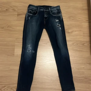 Replay Anbass blå - Snygga Replay Anbass jeans i mörkblå tvätt med slitningar. Klassisk femficksmodell med kontrastsömmar och detaljerade bakfickor. Jeansen är gjorda i stretchigt denim för skön komfort och sitter tajt längs benen. Storlek är 27 waist och 30 Length. Jag säljer dom här byxorna för att jag har växt ur dom. Jag säljer dom för 449+ frakt men pris kan diskuteras. Kontakta mig privat för fler frågor😊