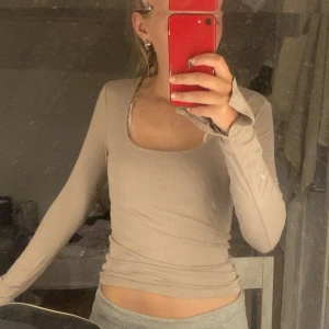 Beige långärmad topp med fyrkantig ringning - Säljer en beige långärmad topp med snygg fyrkantig ringning. Modellen är tight och sitter figurnära, perfekt för dig som gillar en enkel men stilren look. Materialet känns mjukt och stretchigt, vilket gör den skön att bära hela dagen.