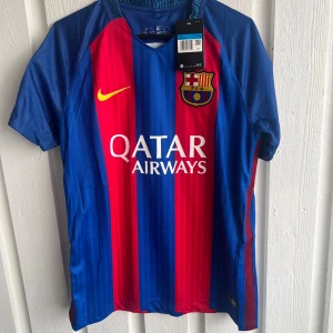 FC Barcelona Messi 10 matchtröja - Säljer en officiell FC Barcelona matchtröja från Nike med Messi 10 på ryggen. Tröjan har klassiska blå och röda vertikala ränder, korta ärmar och klubbmärke på bröstet. Materialet är lätt och andas, perfekt för fotboll eller häng. Snygga gula detaljer och tryck.