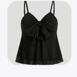 Svart linnetopp med rosett - Supersnygg svart linnetopp med stor rosett framtill och tunna axelband. Toppen har en lätt utsvängd form och är perfekt för att lyfta din outfit. Materialet känns lätt och luftigt, vilket gör den skön att bära. Passar dig som gillar att sticka ut med detaljer.