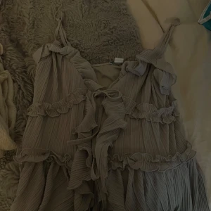 Topp med volanger - Säljer en superfin beige topp  med volanger och plisserade detaljer. toppen har smala axelband och flera lager med volang som ger en romantisk vibe. Prislappen är kvar