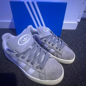 Adidas Campus 00s grå sneakers - Adidas Campus 00s sneakers i grå mocka med vita klassiska stripes på sidorna och vit Adidas-logga på tungan. Skorna har rund tå, platt sula och snörning. Snygg retrostil som passar perfekt till streetwear och chill outfits. Nästan helt nya skulle säga skick 8-9/10 kvitto finns så dem är såklart äkta nypris 1300 skrig vid minsta lilla fundering😀🤗