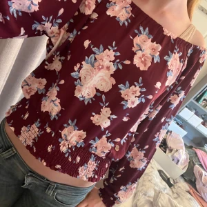 Blommig vinröd blus💓💓 - Supersöt vinröd blus med rosa och blått blommönster. Offshoulder tröja och långa ärmar med smock vid midja och ärmslut. Tillverkad i mjuk polyester som känns skön mot huden. Nästan aldrig använd.💓💓
