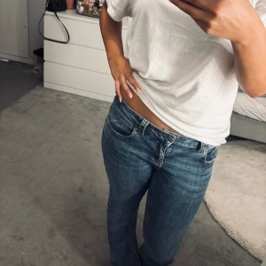 Blå bootcut jeans från gina tricot  - Säljer ett par blå bootcut jeans från Gina Tricot i modellen Perfect Jeans, med låg midja och klassisk femficksdesign. Jeansen har snygga detaljer som knappar på bakfickorna och slitningar för en cool look. Passar dig som gillar en avslappnad och tidlös stil.
