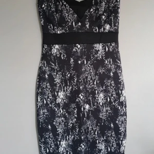 Svart snakeprint klänning Gina Tricot - Snygg svart klänning från Gina Tricot med vit snakeprint och markerad midja. Klänningen har v-ringad hals, slits bak och dragkedja i ryggen. Materialet är mjukt och följsamt, perfekt för dig som vill sticka ut med ett coolt mönster.