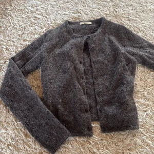 Mörkgrå kofta från Gina Tricot - Säljer en mysig stickad mörkgrå/brun kofta från Gina Tricot i storlek XS. Koftan har rund hals, långa ärmar och knappar framtill. Materialet är stickat och känns riktigt mjukt och skönt mot huden. Perfekt att slänga på sig när det är kyligt ute, värmer extremt mycket! storlek XS och ingår i ginatricots premium sortiment. Helt oanvänd.